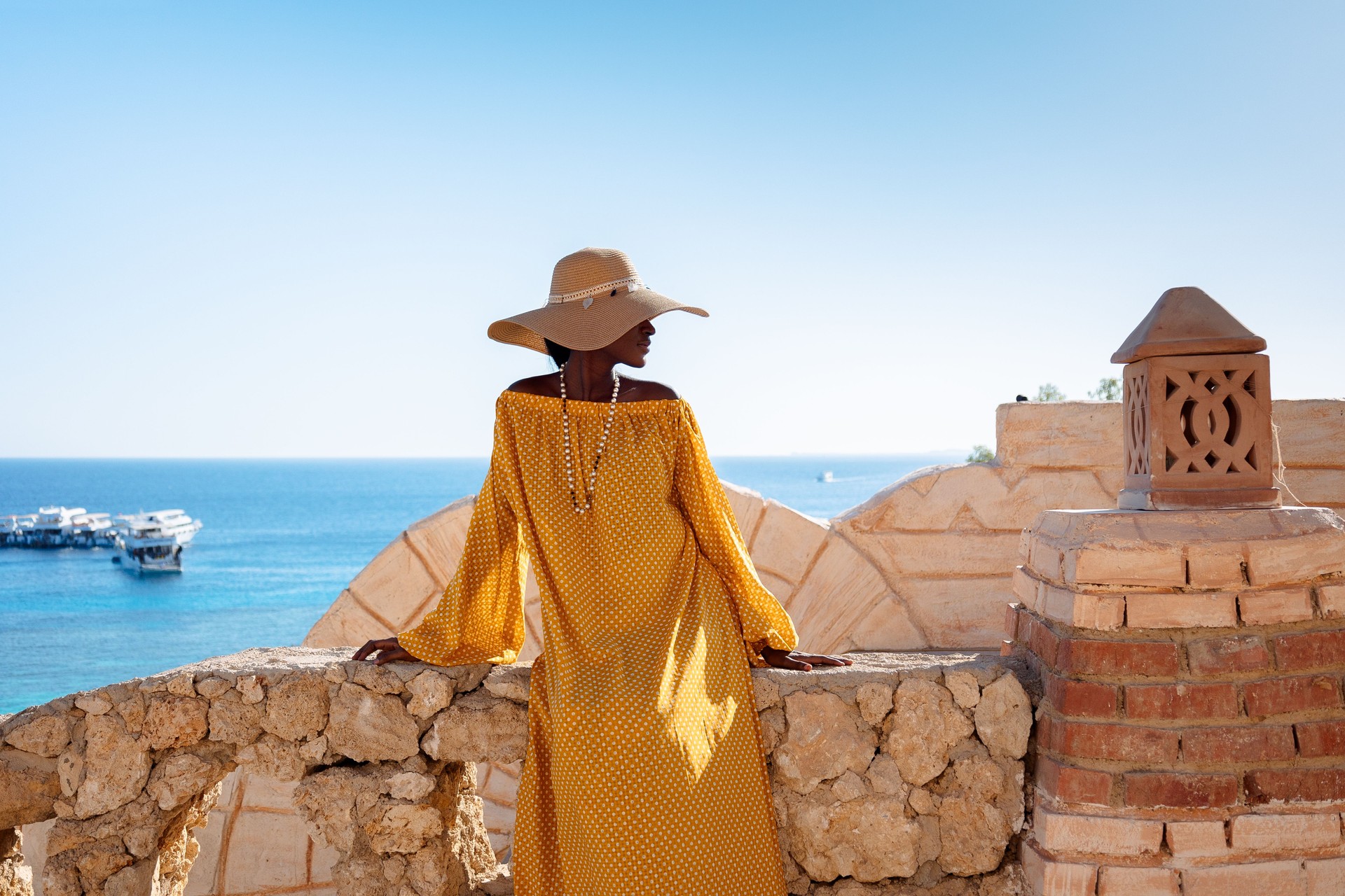 Happy African American Woman In Yellow Dress And Sun Hat Enjoys View Of Coast Of Red Sea On Natural
